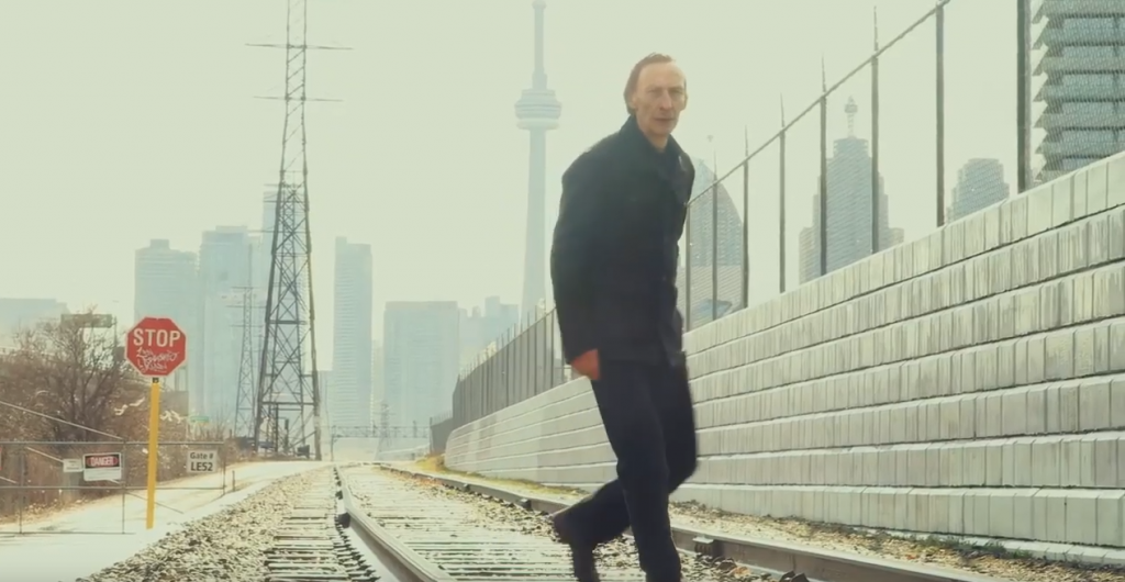 Image tirée de My One Demand, monmtrant l'un des personnages, un homme, sur une voie ferrée, avec la ville en arrière-plan.